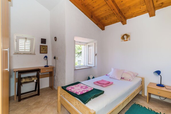A bedroom with a wooden bed, a desk, a chair, a nightstand, and a window.