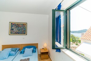 A bedroom with a bed, a nightstand, a lamp, a framed picture, and a window with a view of a building and trees.