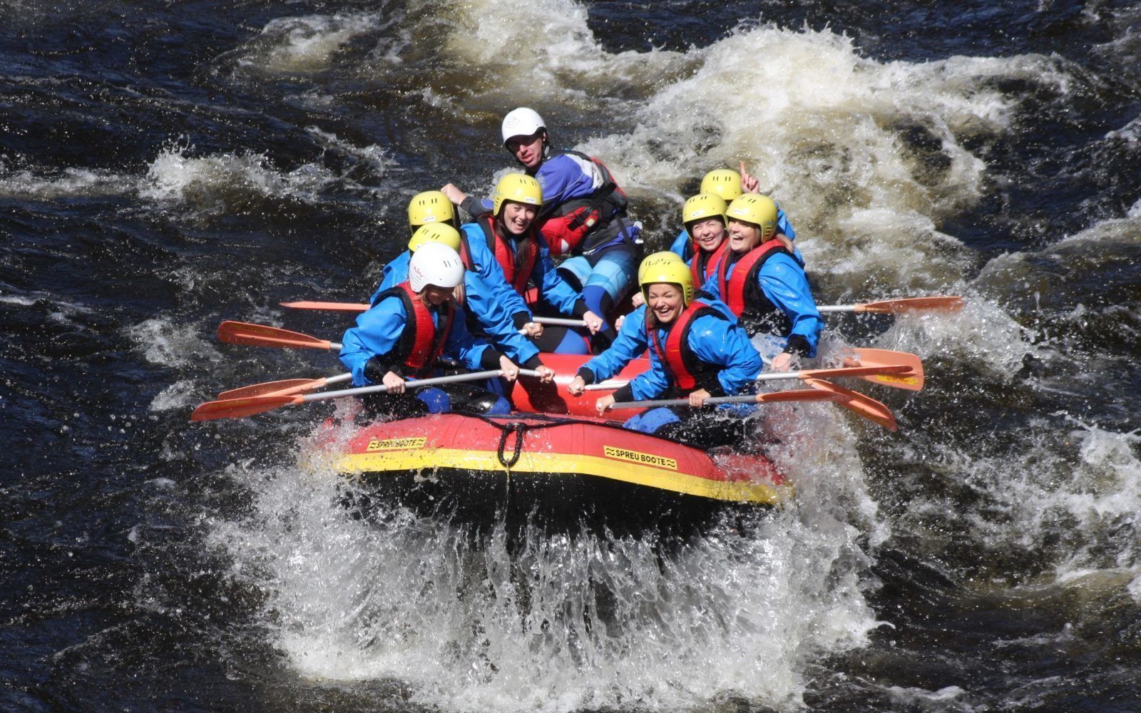 A group of people in a red and yellow inflatable raft navigating through turbulent rapids.