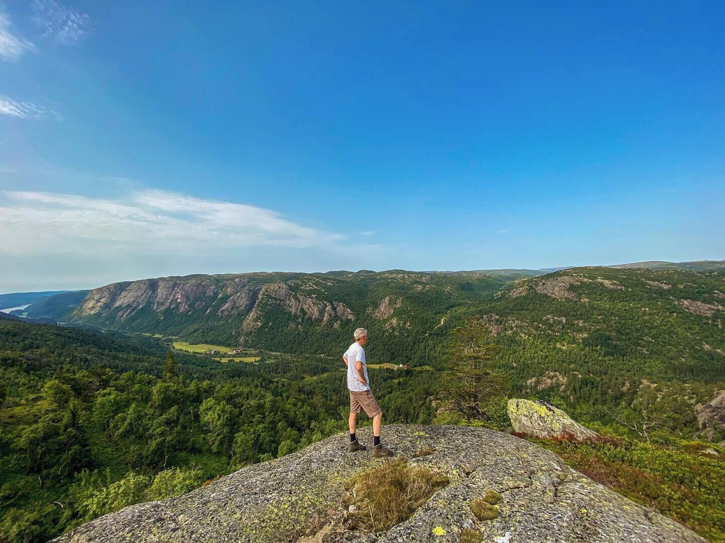 Una persona está de pie sobre un afloramiento rocoso con vistas a un paisaje montañoso.