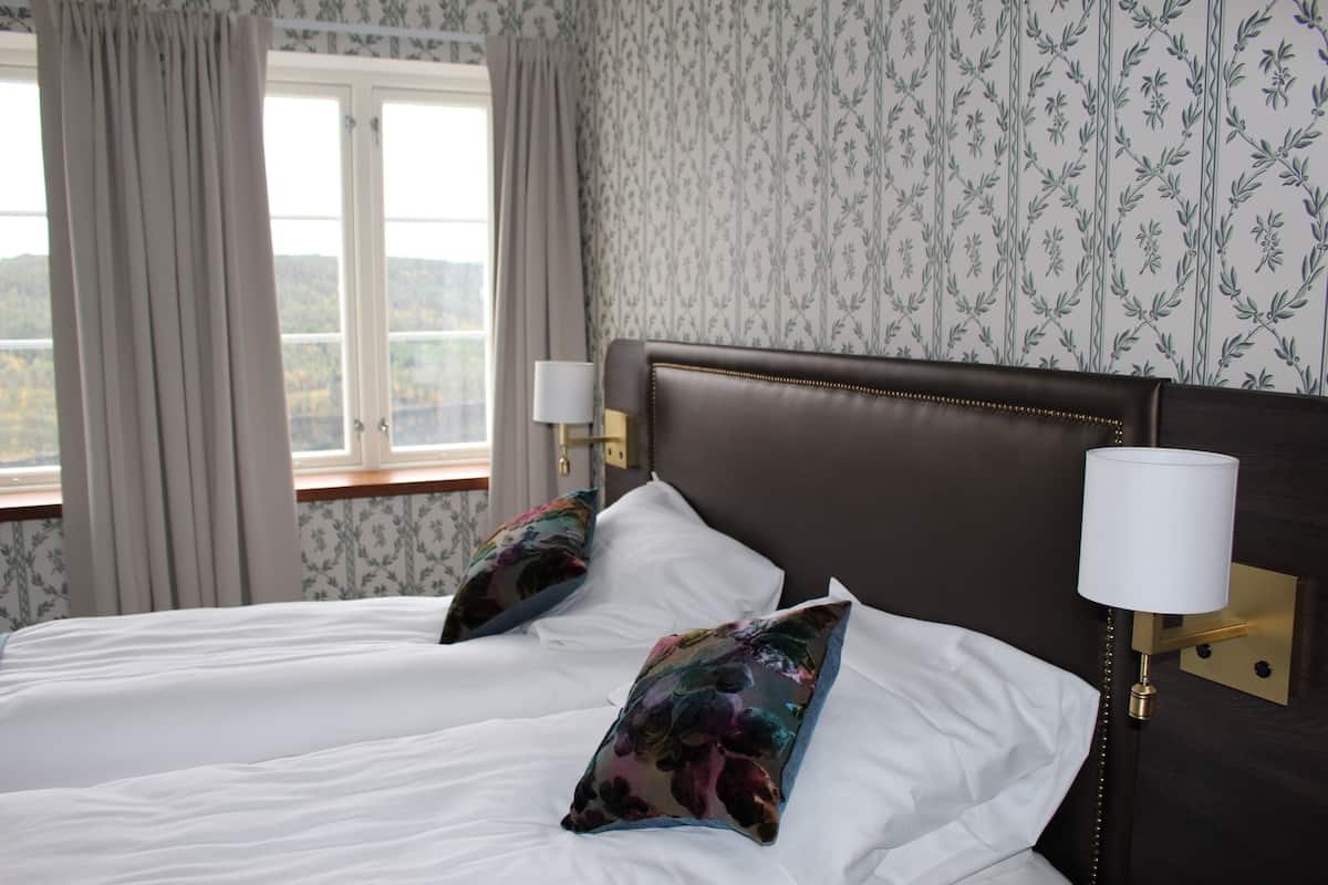 A double bed with floral pillows, a nightstand with a lamp, and a window with curtains.