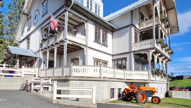 A multi-story building with balconies, a flag, and a parked tractor. - Hotell Eikerapen Gjestegard (Aseral)