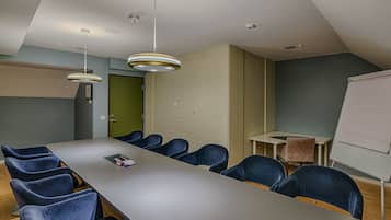 A conference room with a long table, blue chairs, a whiteboard, and pendant lights.