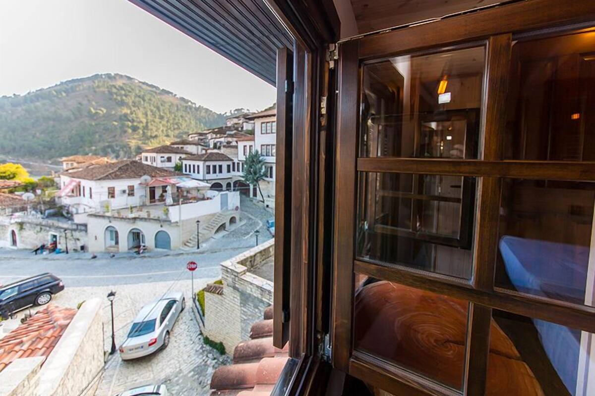 Habitación de hotel con vista a un pueblo en la ladera, una escalera de madera y un coche aparcado fuera.