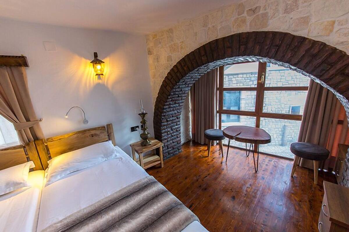 Una habitación acogedora con una cama, una mesita, dos sillas y un arco de piedra que da a una ventana.