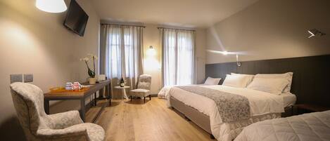 Une chambre d’hôtel comprenant un lit, un bureau avec une chaise, un téléviseur fixé au mur et une fenêtre avec des rideaux.