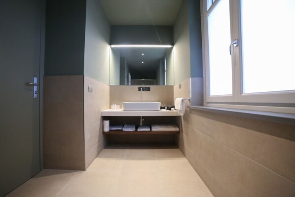 Un baño estrecho con un espejo grande, un lavabo blanco y una ventana en un lateral.