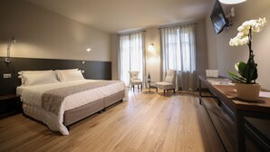 Une chambre d’hôtel avec un lit, deux chaises, un bureau, une télévision et une plante en pot.