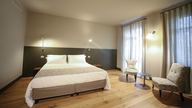 A hotel room with a large bed, two bedside tables, a chair, a small table, and a window with curtains. - Locanda Ferro UNO Golf Città di Asti (Asti)
