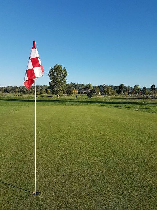 A golf course with a flag on a flagpole, surrounded by green grass and trees. - Locanda Ferro UNO Golf Città di Asti (Asti)