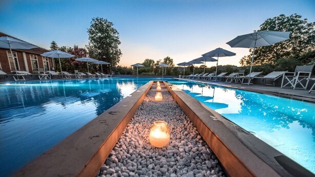 Une piscine entourée d’arbres et d’un bâtiment, avec des chaises longues et des parasols.