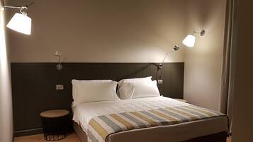 Un letto rifatto con cura, una coperta a righe, due lampade da comodino, un tavolino piccolo e rotondo e un poggiatesta scuro.