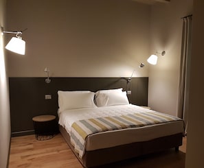 Una cama bien hecha con una colcha a rayas, dos lámparas de noche, una mesita redonda y un cabecero oscuro.