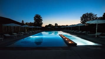 Una piscina con lettini e ombrelloni, circondata da alberi.