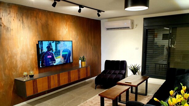 Una sala de estar moderna con televisor de pantalla plana, un sofá oscuro, una mesa de centro de madera y una planta en maceta.