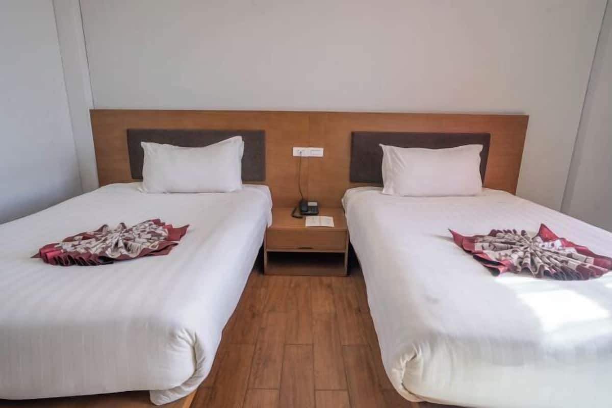 A hotel room with two single beds, wooden headboards, white bedding, and a wooden floor.