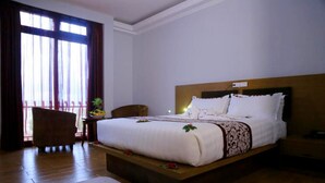 A hotel room with a large bed, wooden flooring, a nightstand, a chair, and a window with curtains. - Haile Resort Gondar (Gondar)