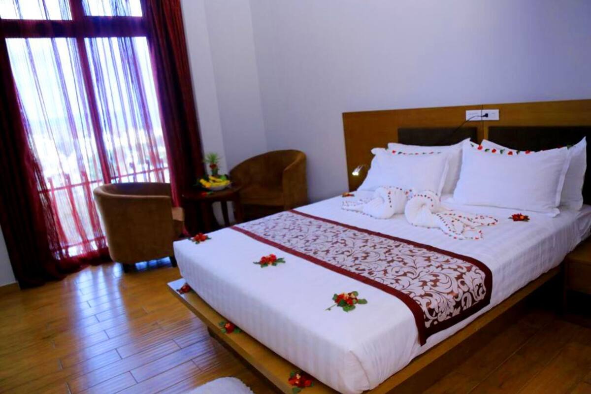 A neatly made bed with white linens and a decorative red and white pattern, a wooden headboard, and a small wooden chair beside the bed.