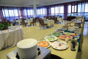 A banquet hall with multiple tables set for dining, large windows, and a buffet line with various dishes. - Haile Resort Gondar (Gondar)