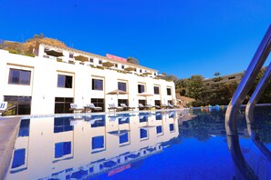 A hotel with a swimming pool, multiple balconies, and sun loungers.