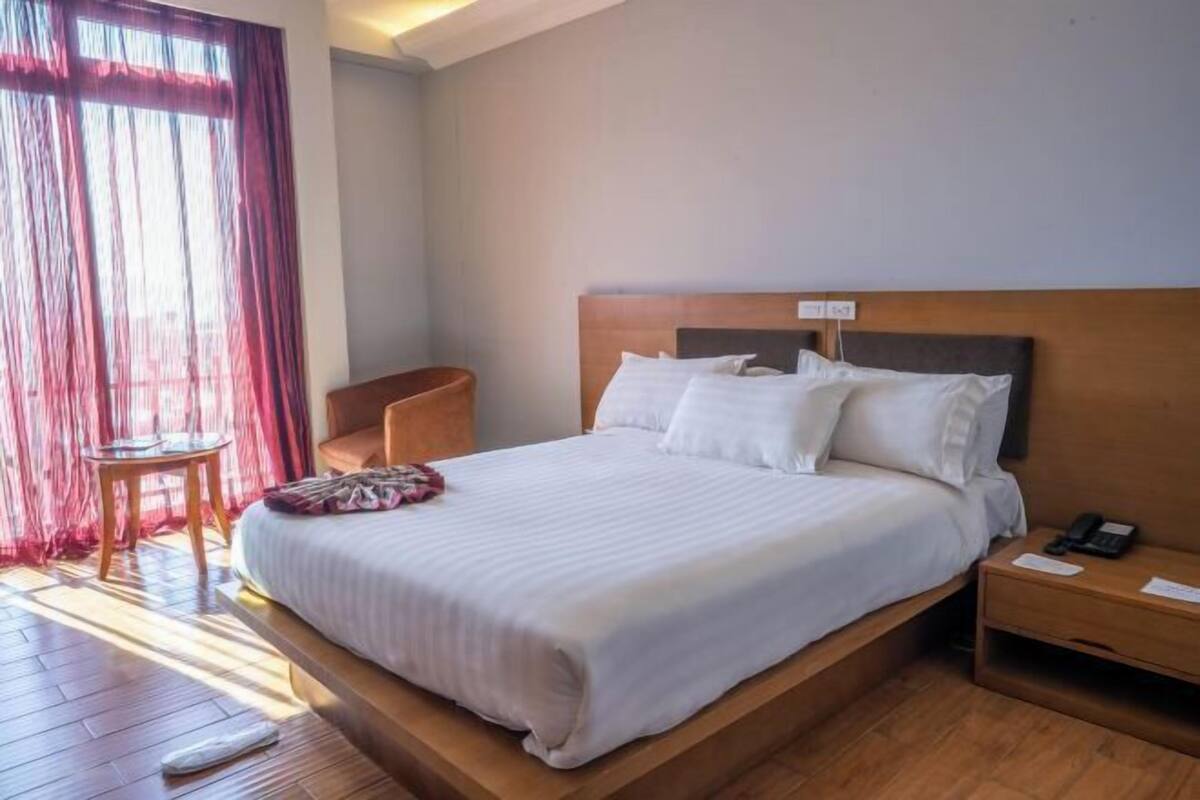 A hotel room with a large bed, a bedside table, a chair, and a window with curtains.