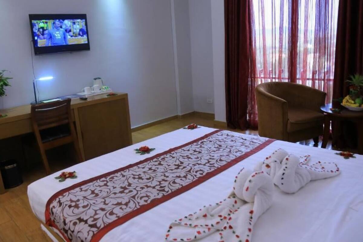 A hotel room with a bed, a desk, a chair, a TV, and a window with curtains.