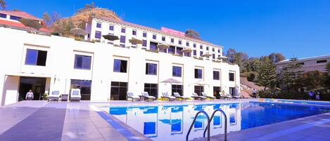 Ein Hotel mit Schwimmbad, mehreren Balkonen und wolkenlosem, blauem Himmel.