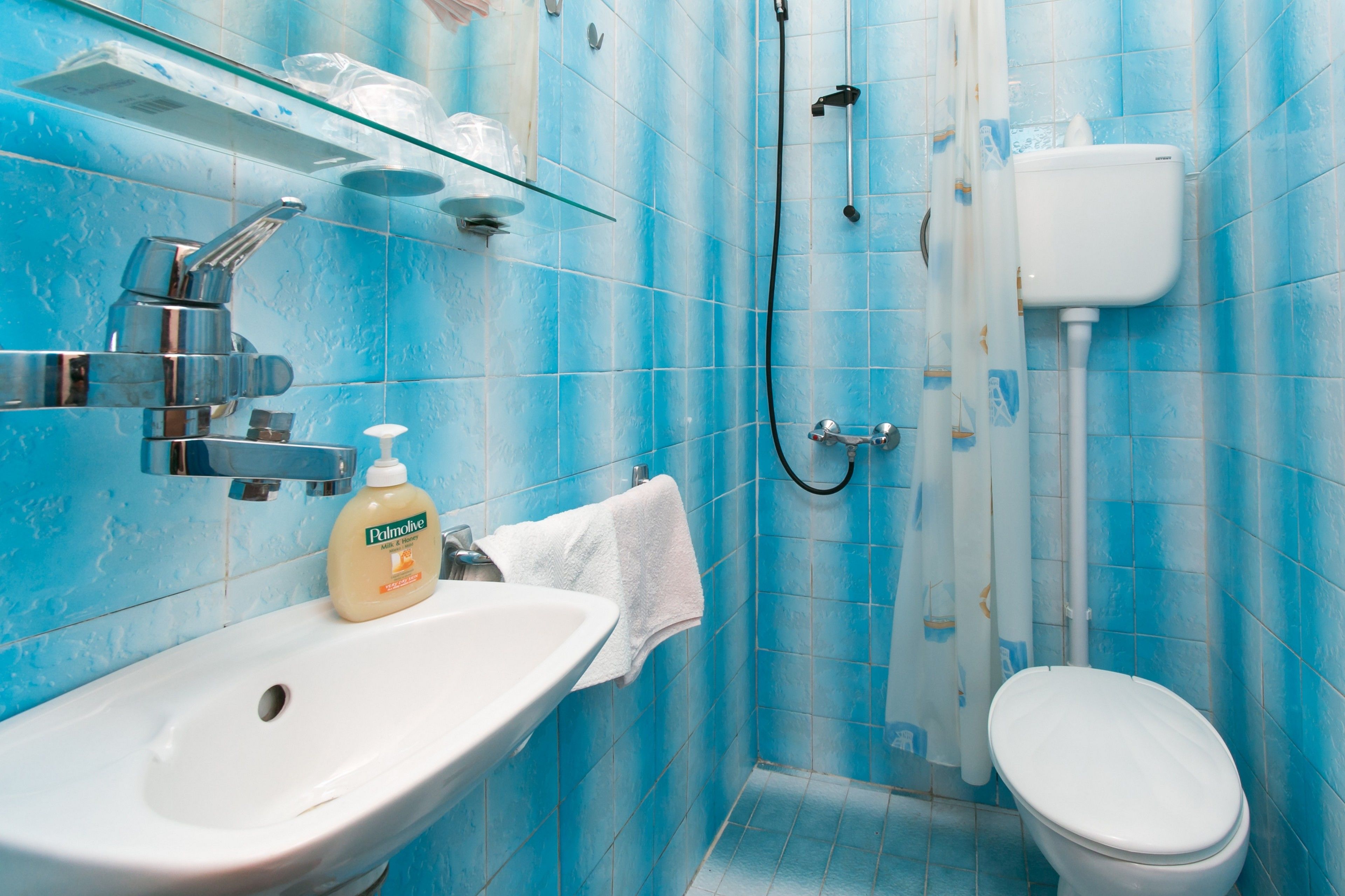 Une salle de bain avec un lavabo blanc, une étagère en verre, des toilettes blanches et des murs recouverts de carreaux bleus.