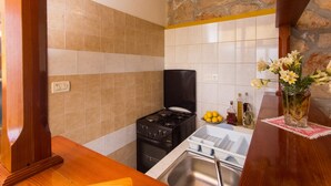 A compact kitchen with a gas stove, a sink, and a stone wall. - Guest House Simunovic (Dubrovnik)
