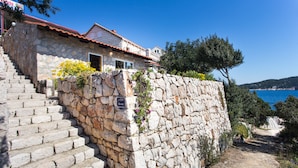 A stone house with a red-tiled roof, a stone staircase leading to a door, and a view of the sea. - Guest House Simunovic (Dubrovnik)