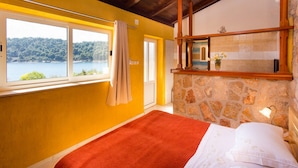 A room with a bed, a stone wall, a window with a view of a lake, and a wooden ceiling. - Guest House Simunovic (Dubrovnik)
