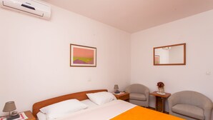 A hotel room with a bed, a nightstand, a chair, a small table with a lamp, and a picture on the wall.