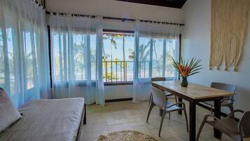 Una habitación con cama, una mesa de comedor con sillas, vistas a la playa y un tapete tejido en el suelo.