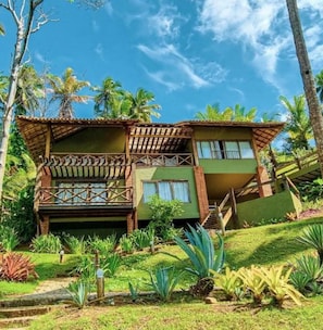 Um edifício de dois andares com varanda, rodeado por vegetação tropical.