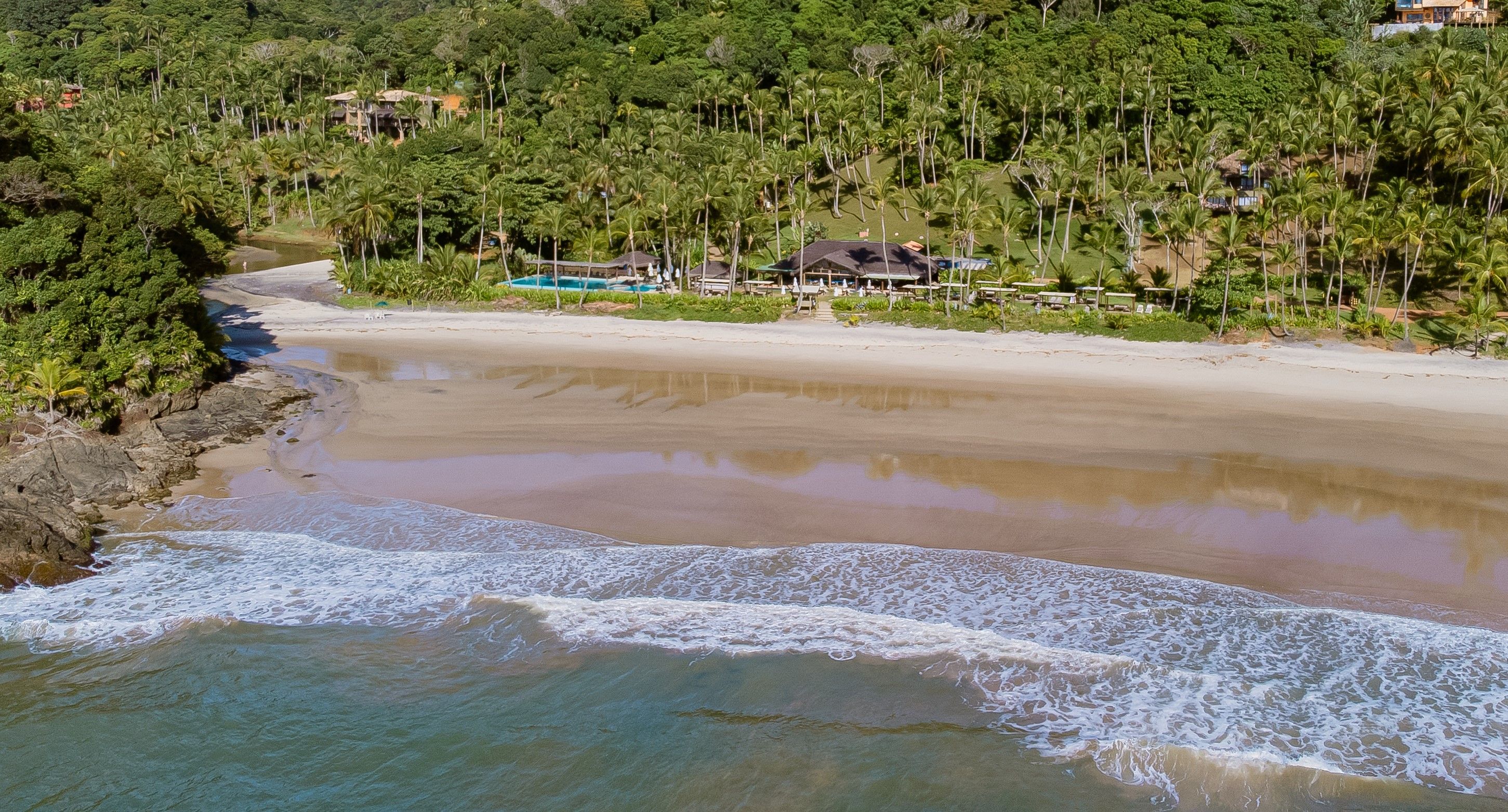 A beach with clear waters, a sandy shore, and a backdrop of dense tropical vegetation.