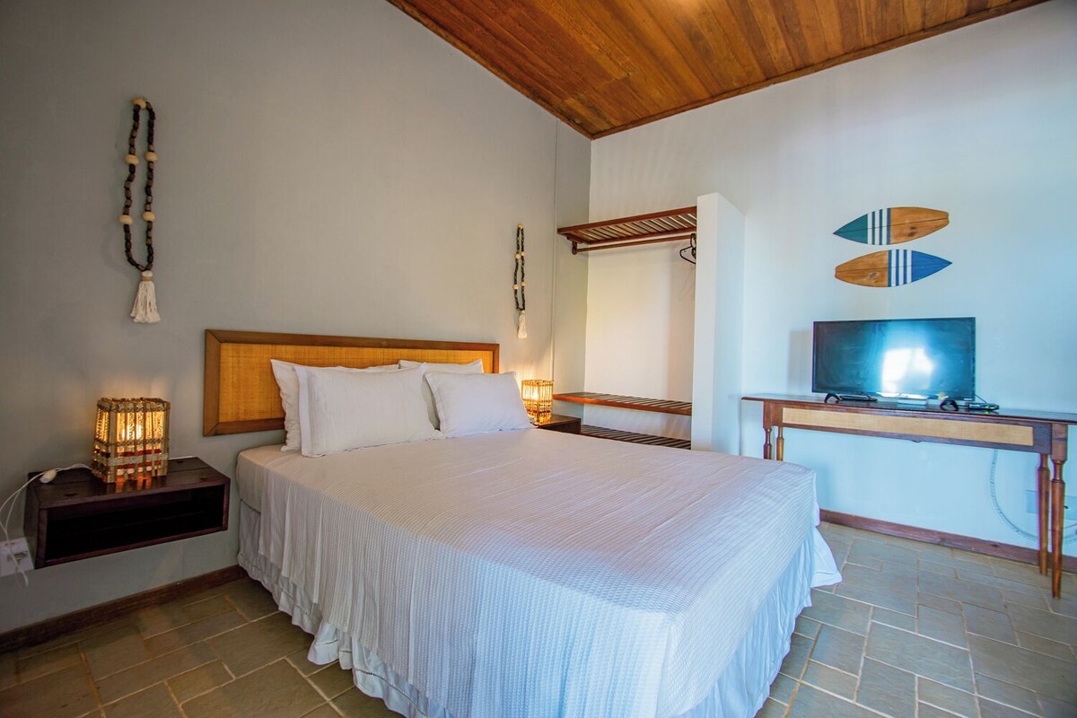 A bedroom with a bed, bedside tables, a TV, and a wooden ceiling.