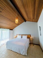 A bedroom with a wooden ceiling, a large bed with white bedding, two bedside lamps, and a small table.
