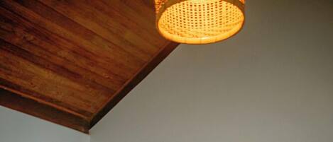 A person sitting on a stool in a room with a wooden ceiling, a microwave, and a bowl of fruit on a table.