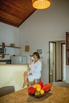 Una persona sentada en un taburete en una habitación con techo de madera, un microondas y un tazón de fruta sobre una mesa.