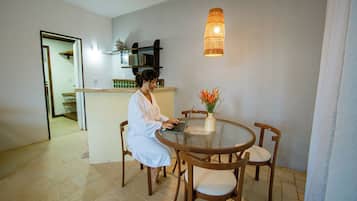 A person seated at a round dining table with a laptop, surrounded by chairs, in a room with a hanging light fixture and a vase with flowers on the table.