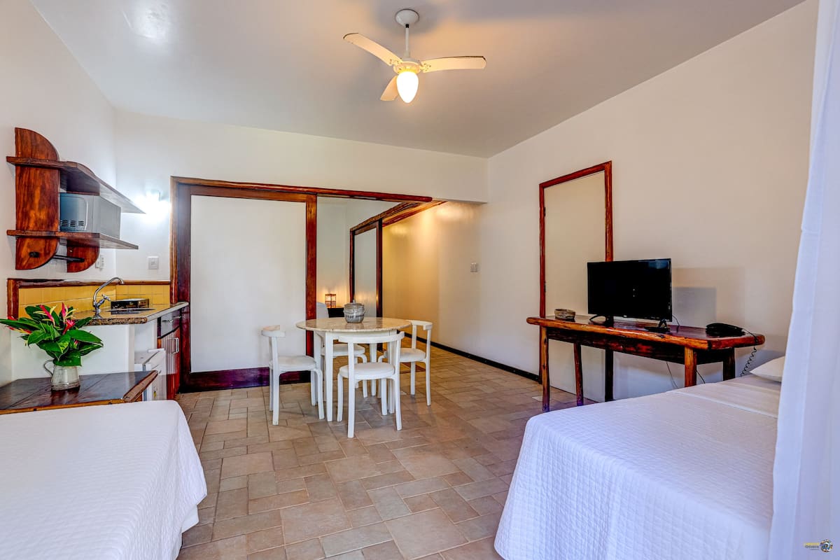 Une chambre d’hôtel comprenant un lit, un bureau avec une télévision, une table à manger avec des chaises, un ventilateur de plafond et un coin cuisine équipé d’un four à micro-ondes.