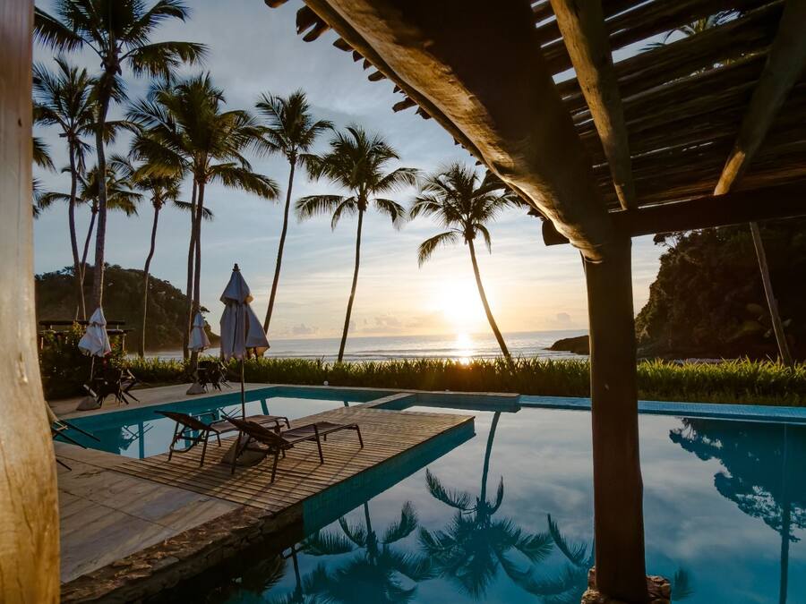 A pool area with lounge chairs and umbrellas, palm trees, and a sunset view.