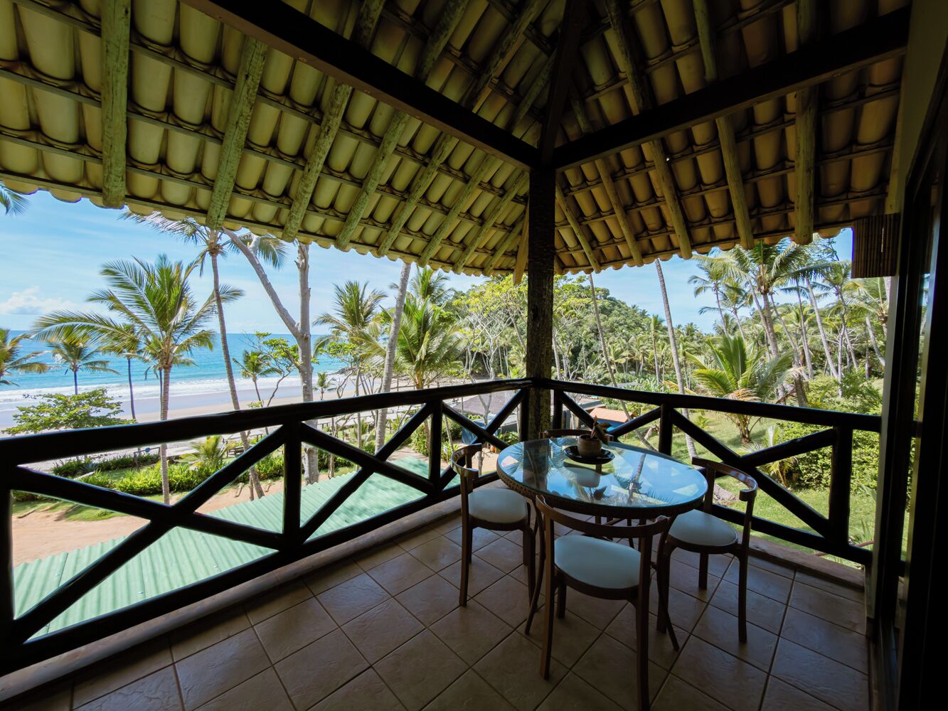 Un espace extérieur aménagé, abrité et doté d’une table et de chaises, offrant une vue sur une plage et des palmiers.