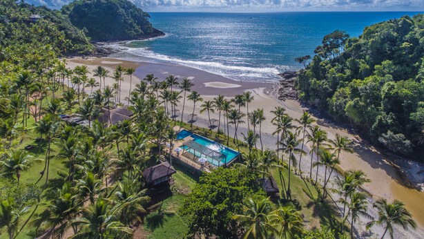 Un resort con piscina, playa y abundante vegetación.