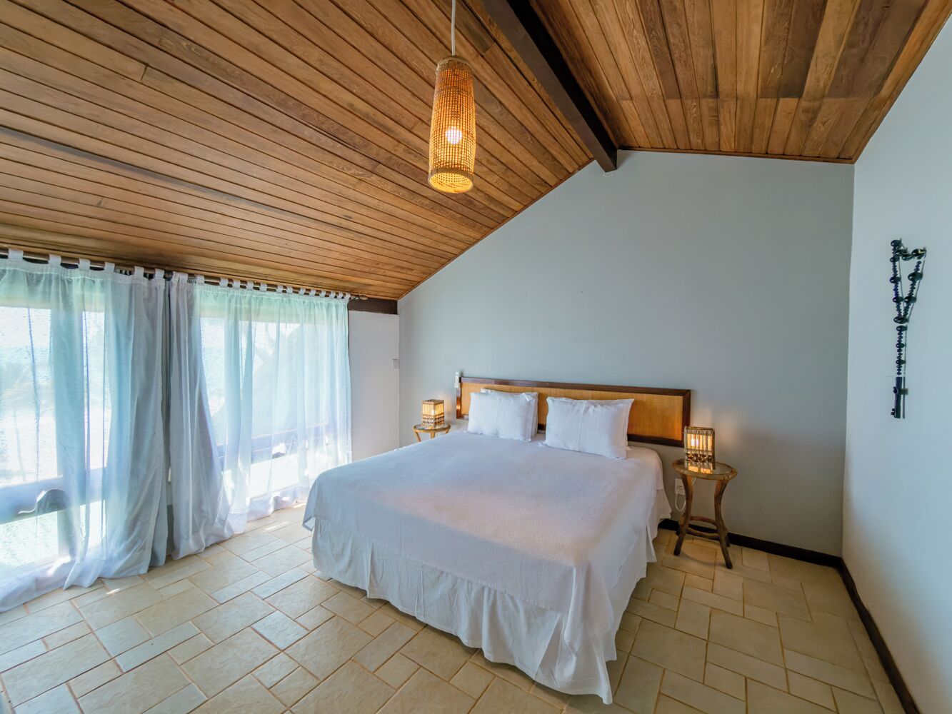 A bedroom with a large bed, wooden ceiling, and a nightstand with a lamp.