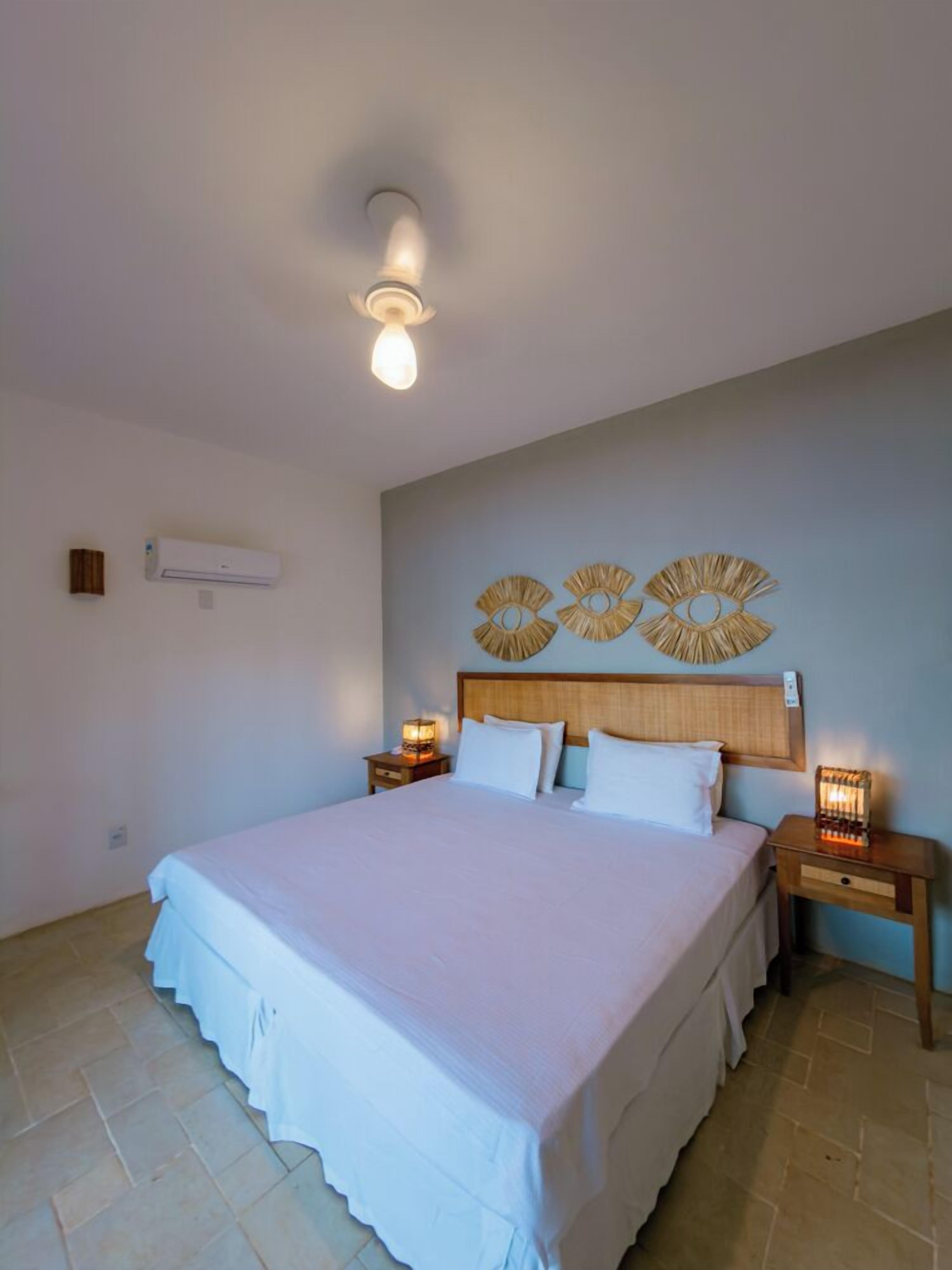 Quarto com uma cama grande, duas mesas de cabeceira com luminárias, uma luz de teto e decoração na parede.