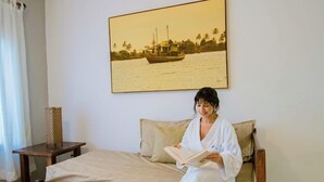 Una habitación con cama, una mesa con jarrones, un cuadro en la pared y una ventana con cortinas.