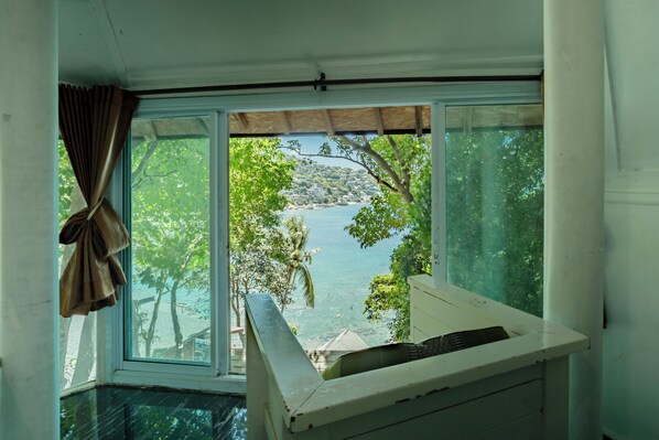 A room with a large window overlooking a body of water and greenery. - Taa Toh Sea View Resort (Koh Tao)