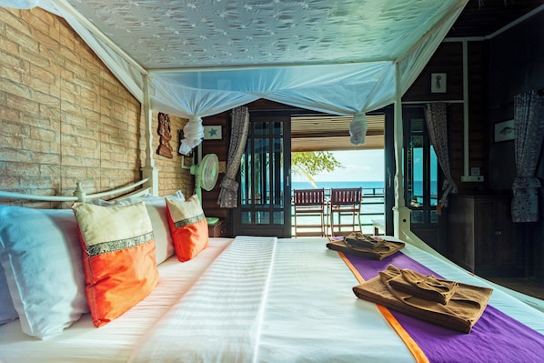 Una habitación con cama, almohadas, ventilador y vista al mar.