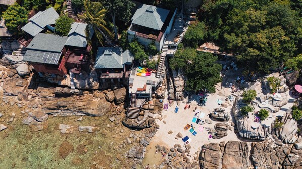 An aerial view of a coastal resort with multiple buildings, a rocky beach, and clear waters. - Taa Toh Sea View Resort (Koh Tao)